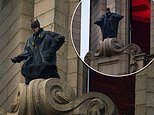 Batman stunt double is strapped to a harness as he leans over Royal Liver Building in Liverpool