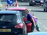 Raging woman spits at driver in the car behind her during argument at a red traffic light 