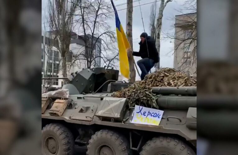 Man jumps on top of armored Russian vehicle while waving Ukrainian flag